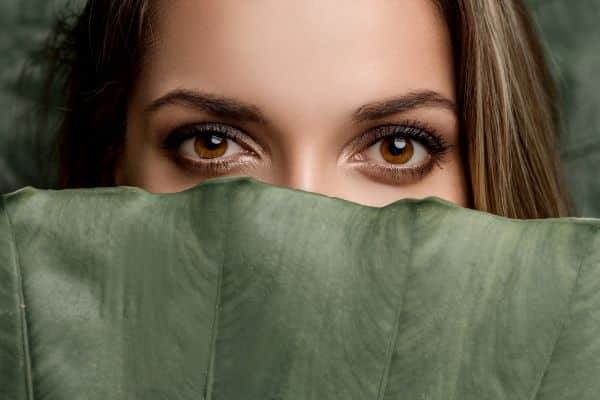 Olhos bonitos de uma mulher destacados atrás de uma folhagem.