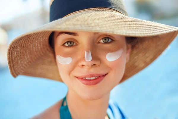 Jovem de olhos claros aplicando protetor solar como forma de prevenção das rugas.