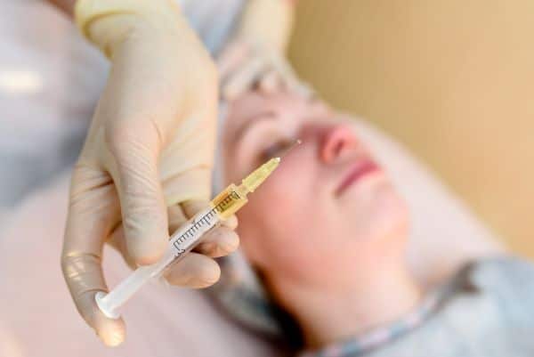 Médico, com a mão enluvada, segurando uma seringa para uso em tratamento estético facial.
