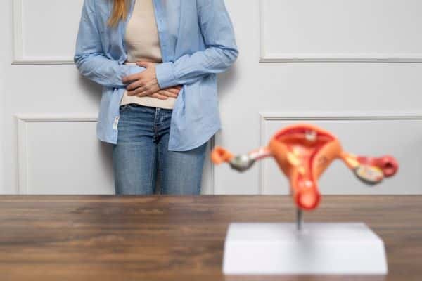 Mulher jovem  com postura indicativa de dor na região do útero.