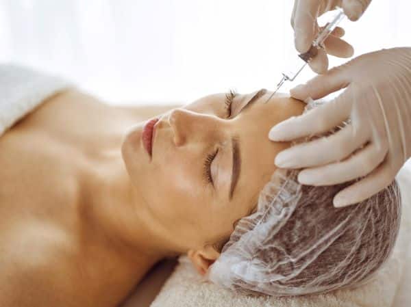 Jovem morena recebendo aplicação de botox na glabela.
