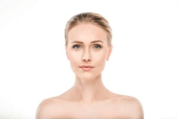 Rosto de uma mulher madura, bonita, com olhos azuis e os cabelos presos. Cuidados com a pele antes e depois de procedimentos faciais.