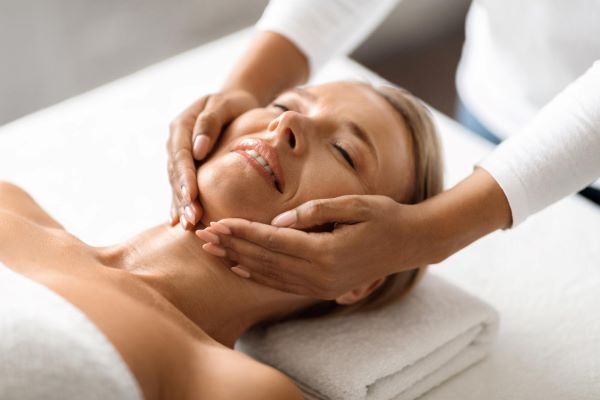 Fisiodermato realiza massagem facial em mulher madura que está deitada na maca.