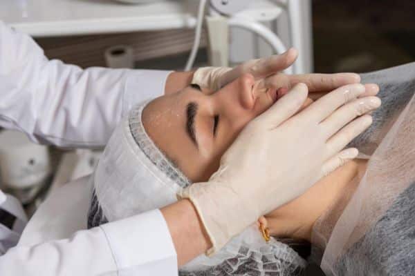 Fisiodermato realizando drenagem linfática facial em paciente que passou por procedimento cirúrgico.