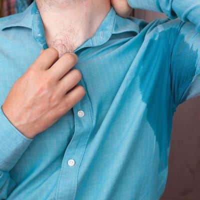 Empresário vestindo camisa social demostra desconforto devido ao excesso de suor, especialmente nas axilas.