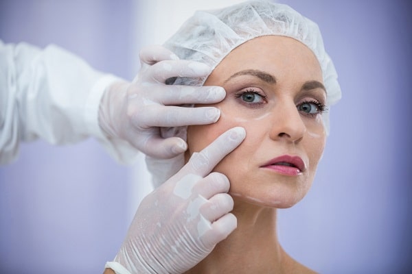 Closão no rosto de mulher madura o qual está marcado para a realização de procedimentos que vão suavizar as marcas do envelhecimento. Médico com luvas brancas analisa o rosto da paciente.