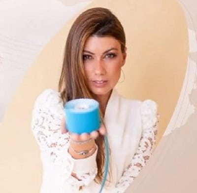 Fisioterapeuta Makssa vestindo um jaleco branco, segura um rolo de bandagem azul para a aplicação do taping no pós-operatório.